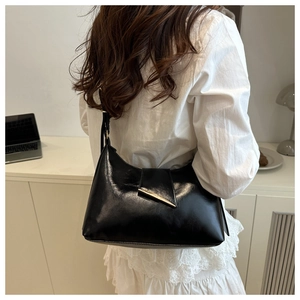 Detail of black glossy leather shoulder bag with a sleek golden metal bar and strap