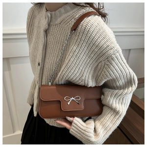 Detail of brown PU leather baguette bag with silver bow buckle and chain strap
