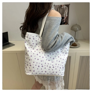 Detail of white tote bag with floral and bow pattern carried by a model in casual setting