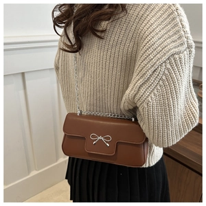 Détail d'un sac bandoulière en cuir marron avec boucle nœud argentée porté par un mannequin