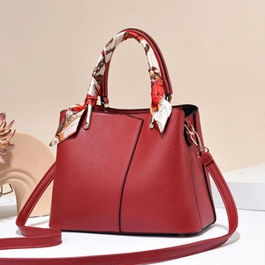 Elegant red leather handbag with scarf-wrapped handle and gold hardware in a 45-degree view