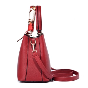 Elegant red leather handbag with floral scarf on handle and gold hardware on white background