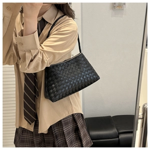 Detail view of a black woven leather square bag worn by a model in a minimalist setting