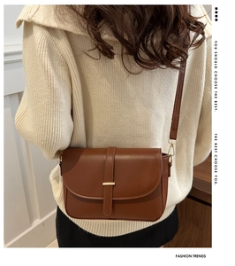 Dettaglio borsa a tracolla marrone con fibbia dorata su un maglione di maglia beige