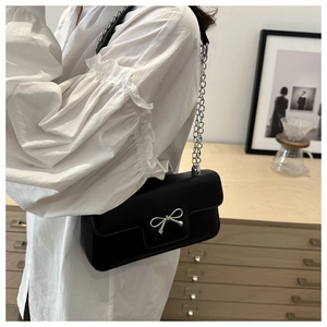 French style black PU shoulder bag with silver bow accent worn by a model in casual setting