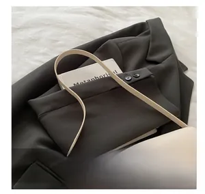 Detail of minimalist cream baguette bag with golden lock on grey blazer and book