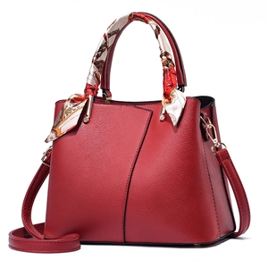 Elegant red leather handbag with lychee texture and decorative silk scarf on handle