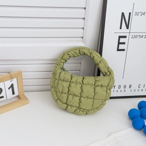 Détail du sac à main matelassé vert clair avec texture bouffante sur un bureau blanc