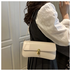 Detail of cream baguette underarm bag with gold oval clasp on an elegant model