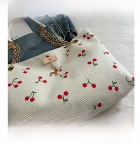 Detail of white corduroy tote bag with red cherry print and golden deer charm