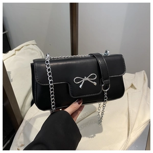 Detail of black faux leather shoulder bag featuring a silver metal bow and chain strap