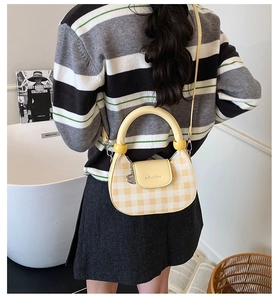 Detail of a yellow and beige plaid crossbody bag with a round handle and brand logo