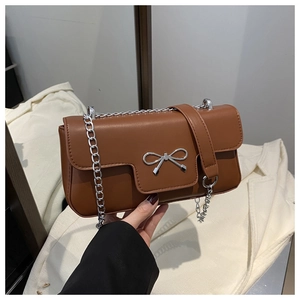 Detail of caramel brown matte leather handbag with silver bow accent and chain strap