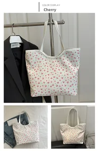 Detail of floral tote bag with red cherry prints and white shoulder straps in a bright setting