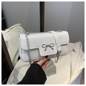 Detail of silver metallic bow on a white polished leather crossbody chain bag