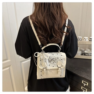 Close-up of white lace backpack featuring black bow patterns and pearl pendant detail