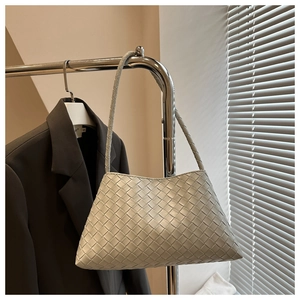Detailed close-up of woven leather texture on a minimalist beige shoulder bag