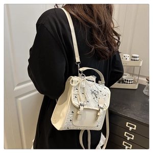 Close-up of cream lace backpack with pearl bow charm and black bow embroidery detail
