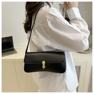 Detail of minimalist black underarm bag with gold oval clasp on model in office