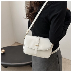 Borsa a tracolla bianca lucida con finiture dorate indossata da una modella in stanza minimal