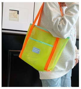 Detail view of neon mesh tote bag featuring orange handles and blue logo patch