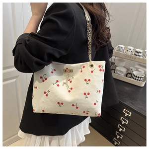 Detail of off-white corduroy tote with cherry print and golden deer charm on chain