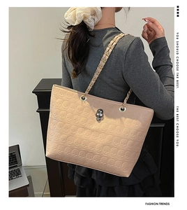 Detail of beige tote bag with embossed skull patterns and silver metal hardware