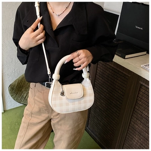 Detail view of a beige checkered crossbody bag with round handle on a minimalist model