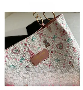 Close-up of white pleated tote bag featuring cartoon prints and gold circular handle