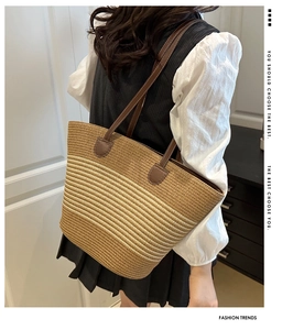 Détail du sac cabas en paille tressée à rayures avec bandoulière en cuir brun sur l'épaule