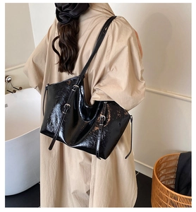 Detail of vintage black patent leather tote bag with adjustable strap on a beige coat