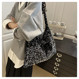 Detailed view of black sequined tote bag worn by a model in a minimalist modern setting