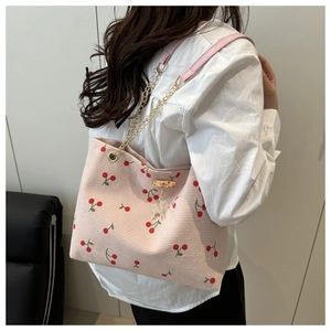 Detailed texture of pink corduroy tote bag featuring red cherry patterns and gold chain