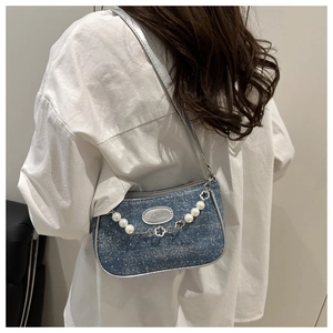 Detail der blauen Denim-Umhängetasche mit Perlenkette und silberner Modeplakette