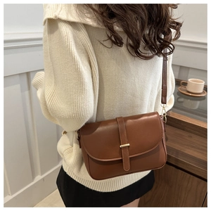 Dettaglio borsa a tracolla marrone con barra dorata indossata su maglione beige