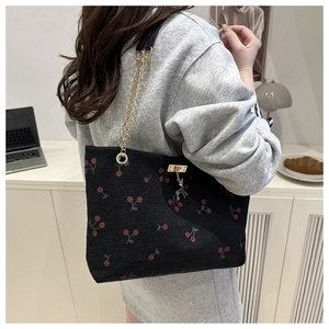 Detail of floral tote bag featuring red cherry print, corduroy texture, and gold chain strap