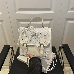 White pleated backpack with pearl bow and lace detail on a minimalist black chair