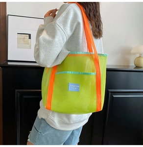 Neon green mesh beach bag with orange straps shown on shoulder for size reference