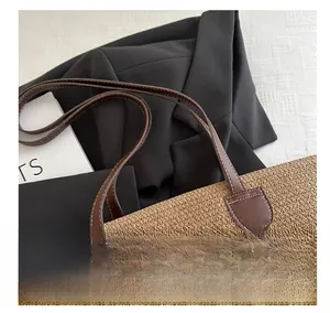 Détail d'un grand sac en paille tressée avec anses en cuir marron sur fond sombre