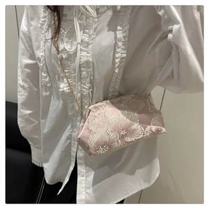 Detail of floral embroidery and gold chain on lavender crossbody bag worn by model