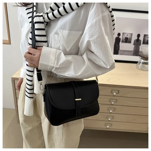 Dettaglio di una borsa a tracolla in pelle nera con fibbia dorata su un outfit camicia bianca