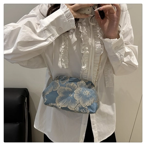 Detail of light blue silk embroidery crossbody bag with golden floral patterns and chain
