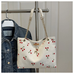 Detail of corduroy tote bag featuring red cherry print and golden deer pendant