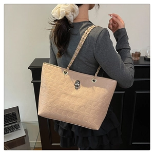 Detail view of embossed skull pattern and metallic skull charm on the beige tote bag
