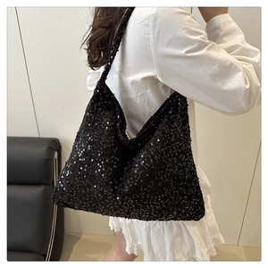 Detail of a large black sequin Hobo bag on a model wearing a white ruffle dress