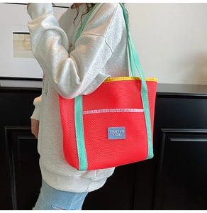 Red and mint green mesh beach bag worn by a model in a minimalist indoor setting