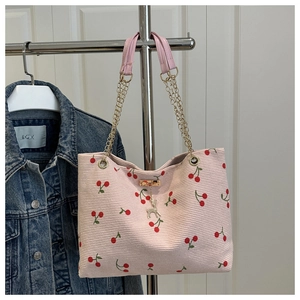 Detail of pink corduroy tote bag with cherry print, gold chain strap and deer charm