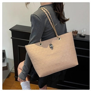 Detail of beige tote bag with skull embossed texture and metal chain strap on woman