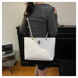 Detail of white tote bag featuring embossed skull textures and silver skull metal hardware