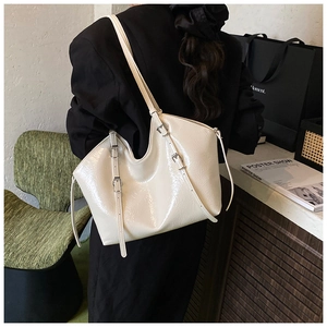 Glossy cream tote bag with metal buckles shown on shoulder against a lifestyle background